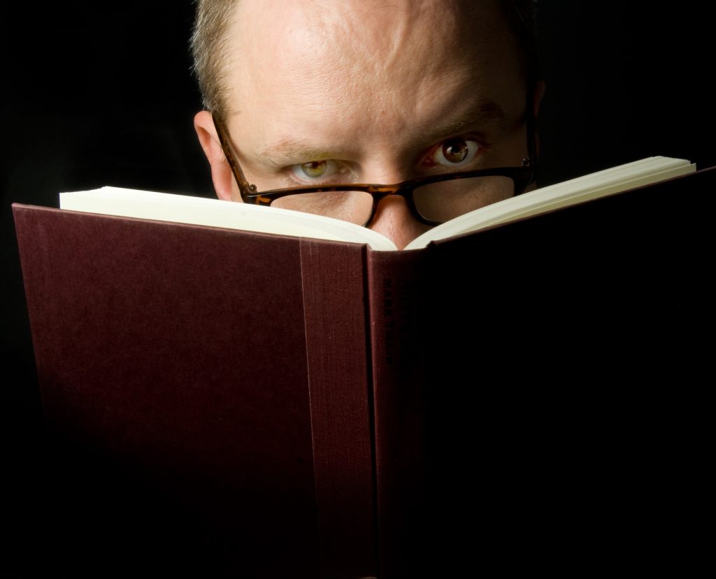Man with glasses holding book in front of face
